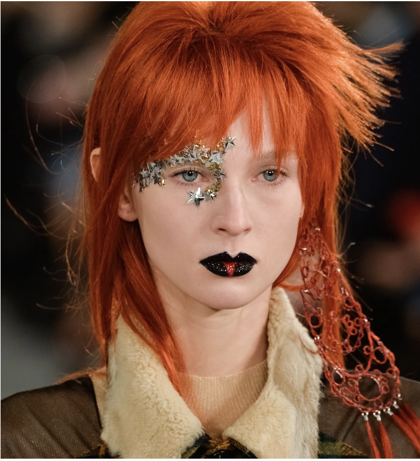 Runway model with copper mullet, silver star sequins around one eye and black glitter lips
