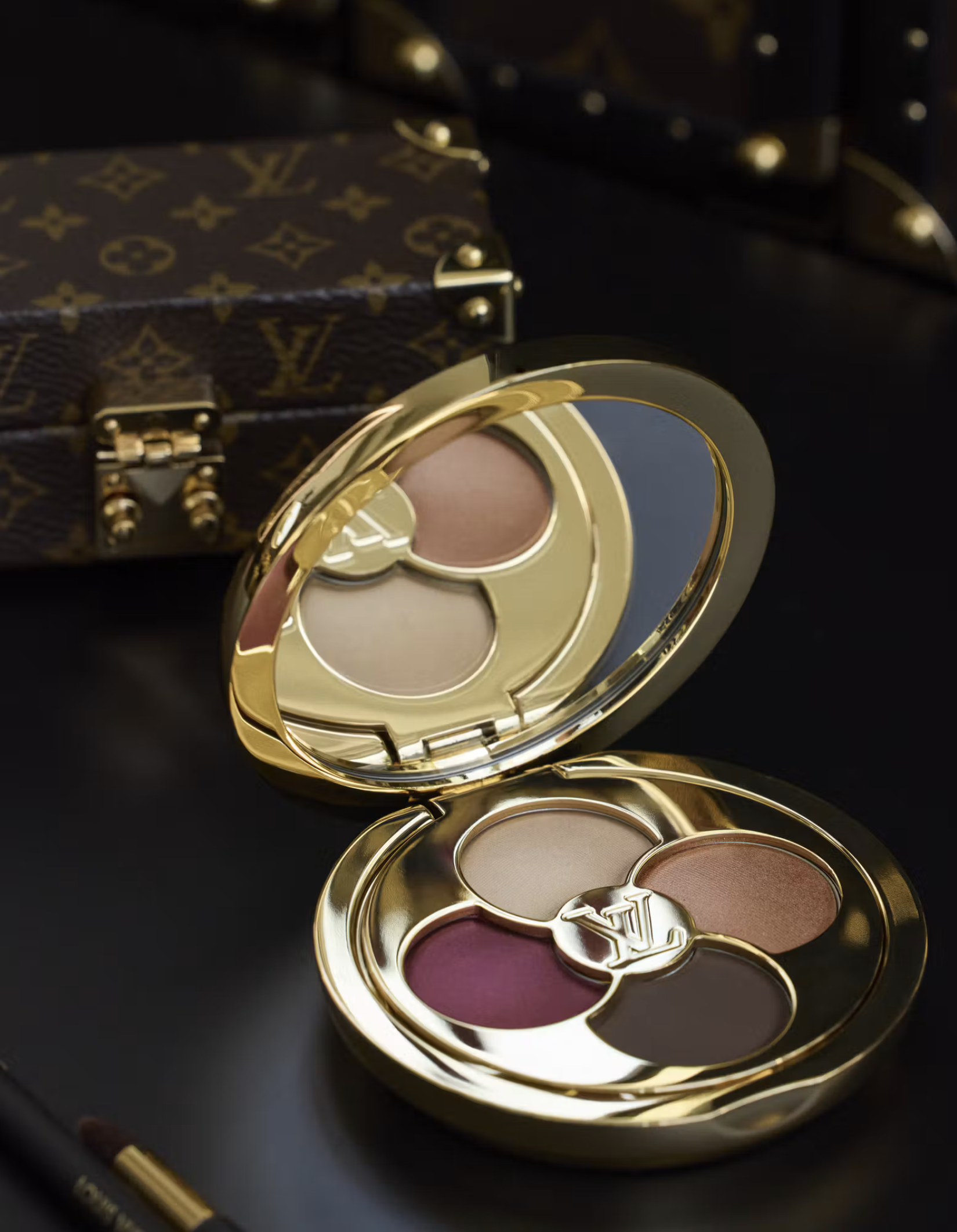 Gold La Beauté Louis Vuitton eyeshadow quad in front of a monogram vanity trunk