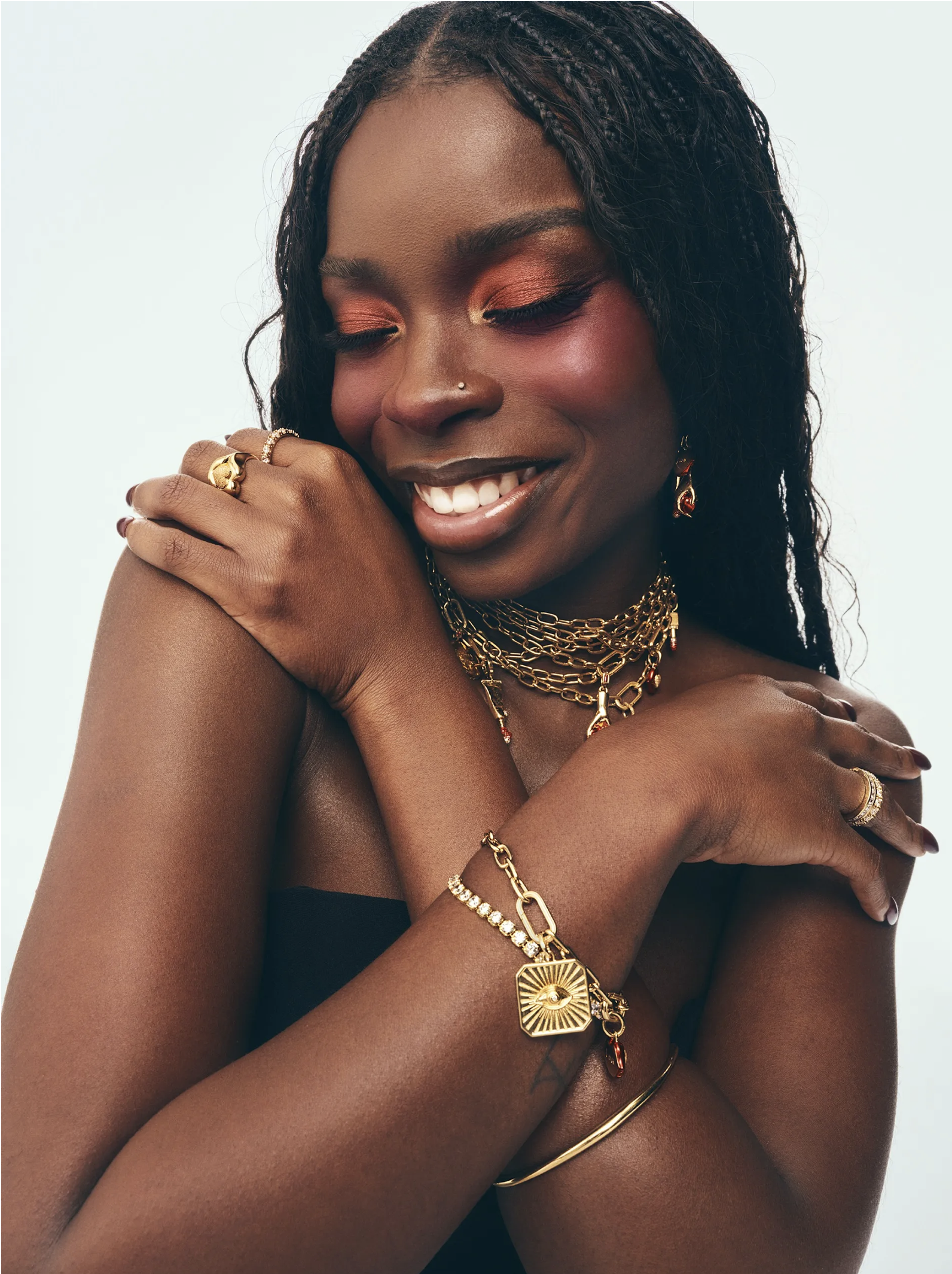 Smiling woman in copper eyeshadow wearing layered gold chains, charm bracelets and lip signet rings